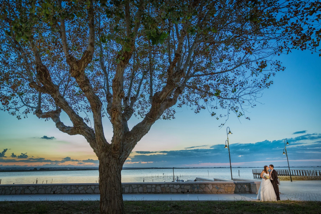 Sposi al tramonto sotto un albero ed il lago di sfondo.
