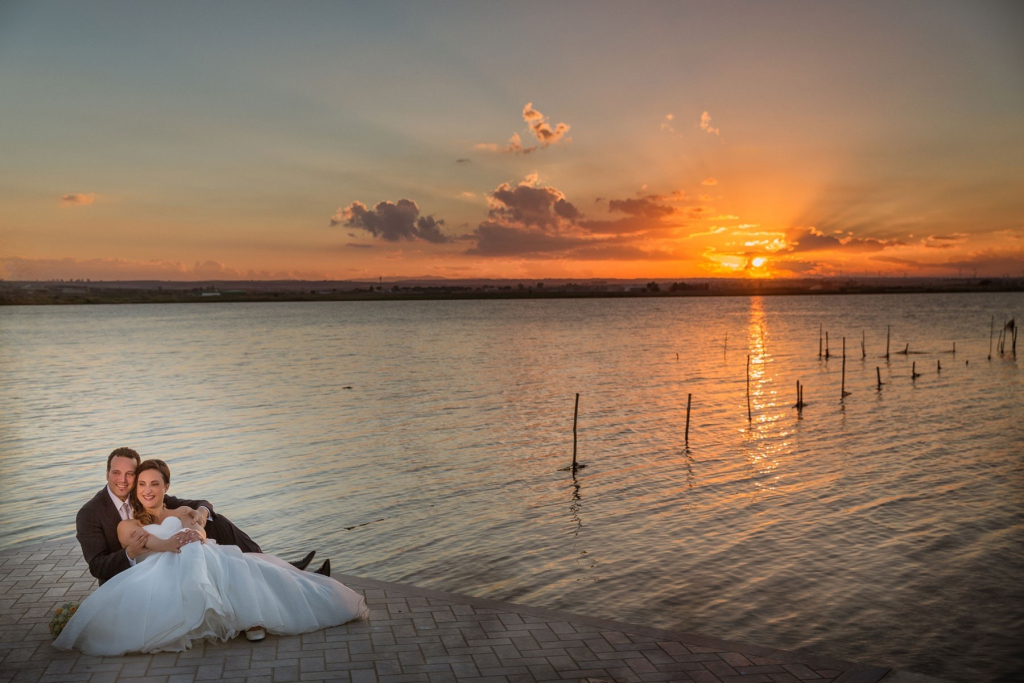 Sposi seduti su molo al tramonto con sfondo il lago.