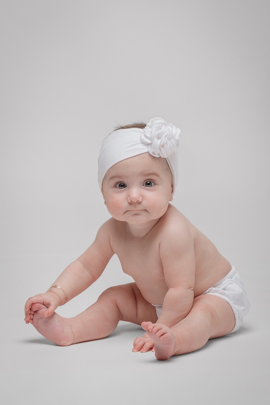 Fotoritratto di neonata con fascia in testa con una rosa