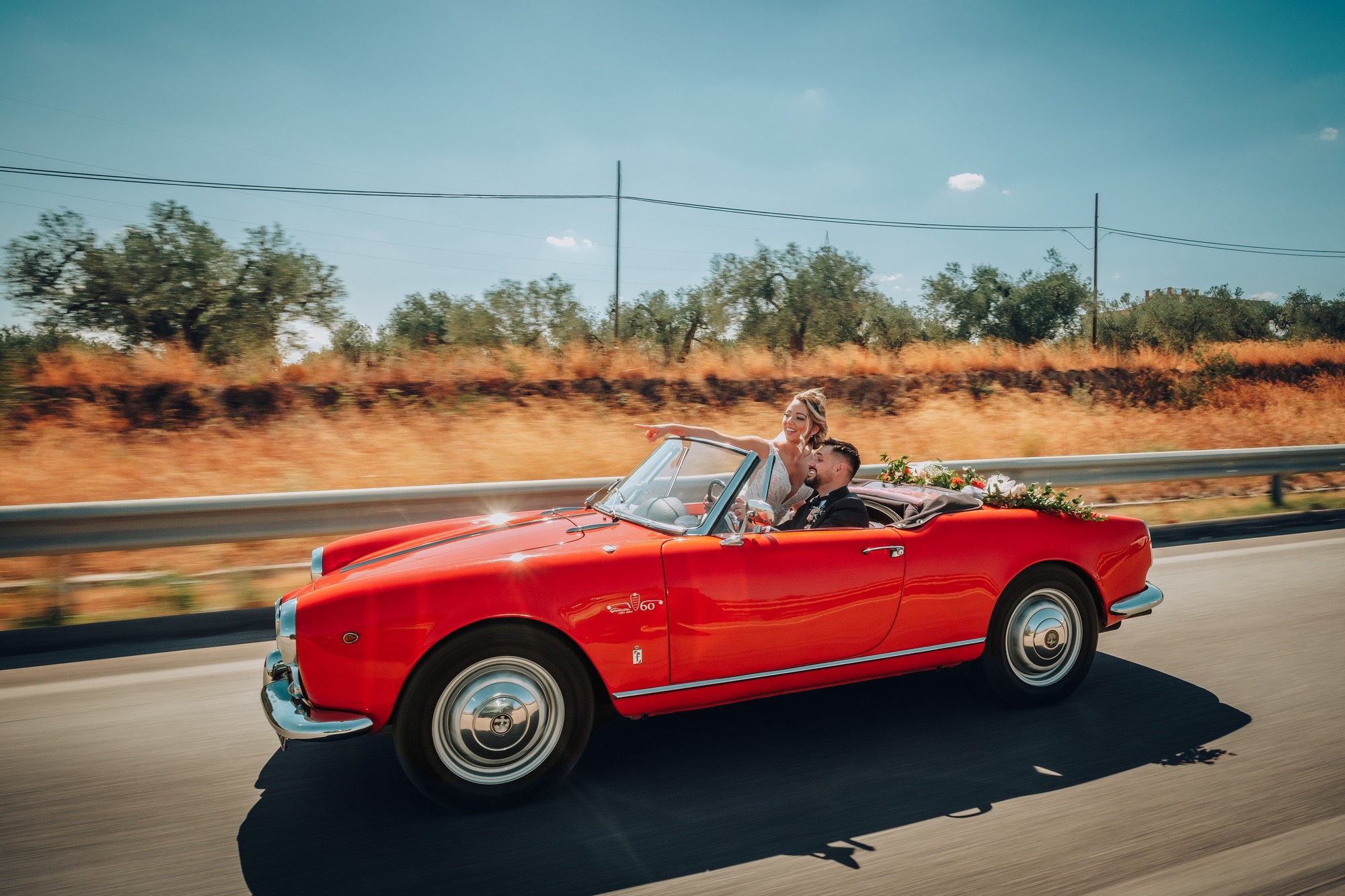 Scatto in movimento di una coppia di sposi su un'auto sportiva rossa.