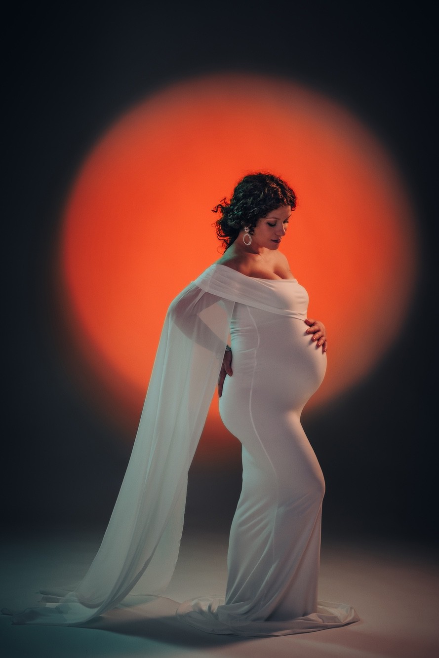 Ritratto donna incinta Ritratto maternità in studio, donna incinta in abito bianco su fondo caldo arancione.