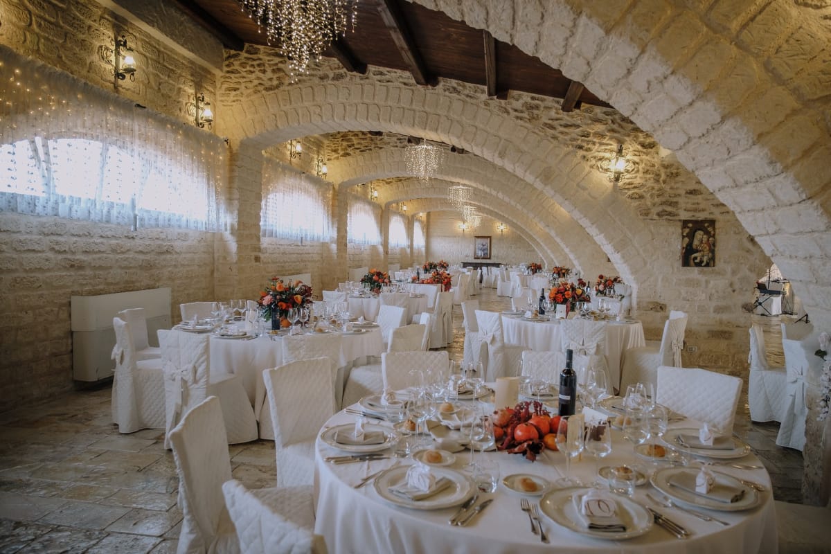 Interno ad archi in pietra viva con tavoli apparecchiati per matrimonio.