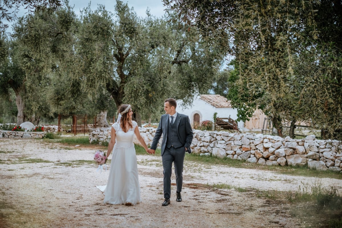 Foto di sposi all'esterno con muretto a secco in pietra ed ulivi.