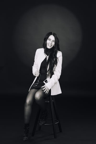 Ritratto professionale di una manager con trench beige e occhiali su sfondo blu, fotografia che racconta ruolo, stile personale e affidabilità oltre il semplice volto