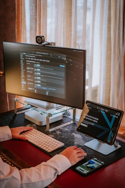 Postazione di lavoro in azienda con monitor, tablet e smartphone, mani del professionista alla tastiera, esempio di fotografia ambientata che racconta contesto e modalità di lavoro