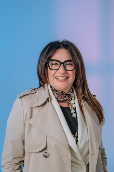 Ritratto professionale di una manager con trench beige e occhiali su sfondo blu, fotografia che racconta ruolo, stile personale e affidabilità oltre il semplice volto