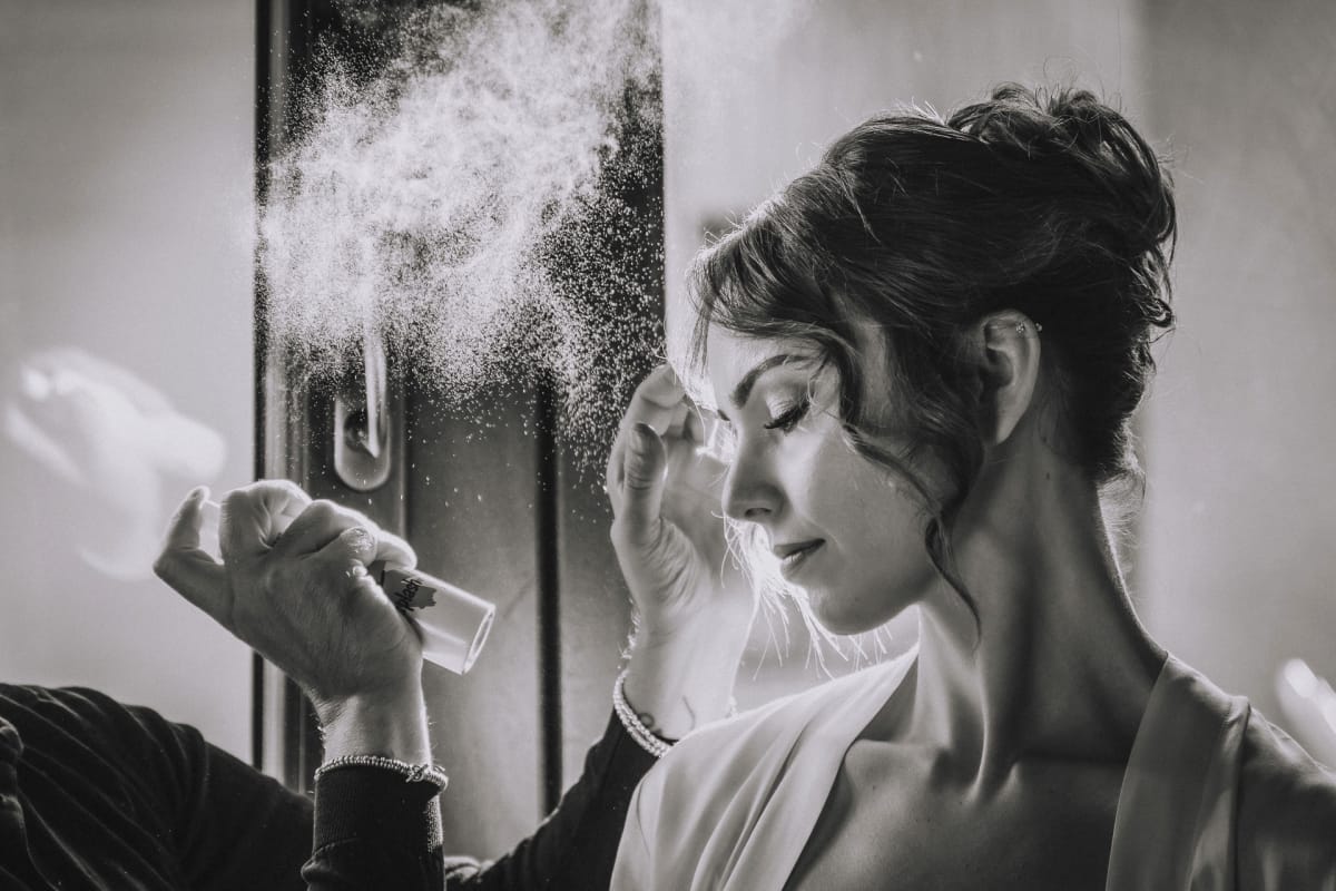 Scatto in bianco e nero della sposa che si protegge il viso mentre le viene fissata l'acconciatura con lo spray