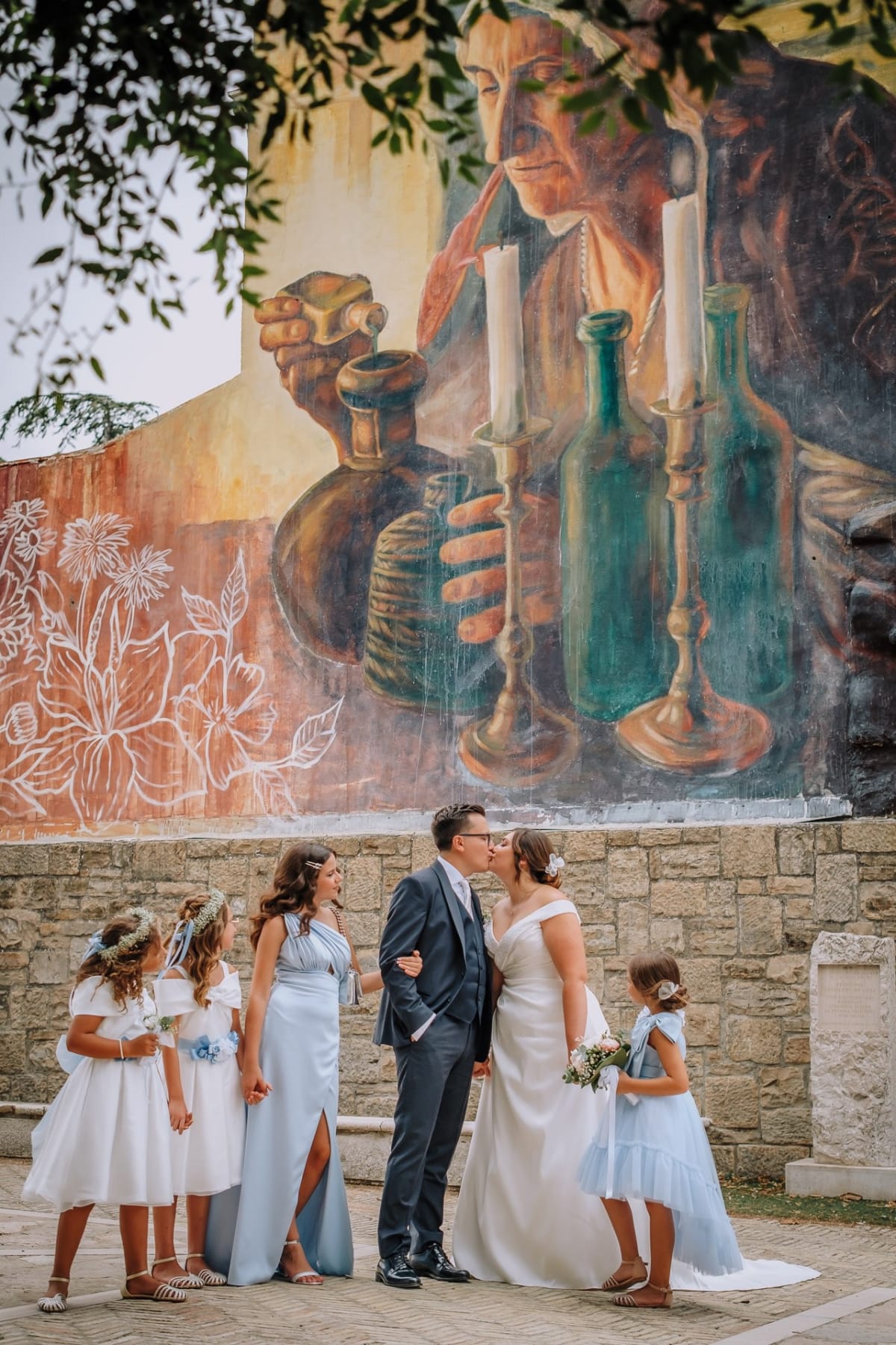 Gli sposi si baciano circondati dalle damigelle, davanti a un grande murale dipinto su una parete